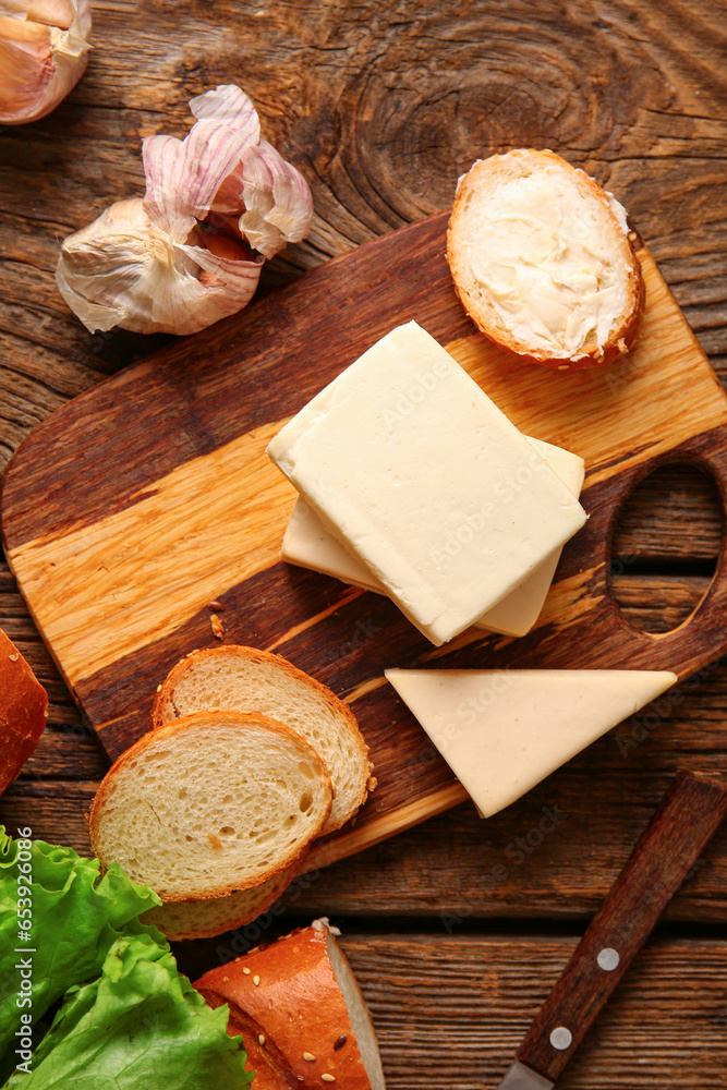 Board with processed cheese, bread and garlic on brown wooden background