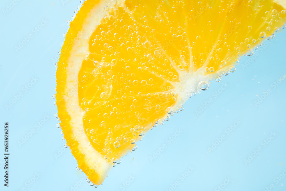 Orange slice in water with bubbles on blue background