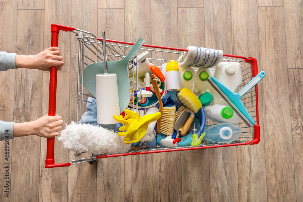 Woman with shopping cart full of cleaning supplies on wooden floor, top view