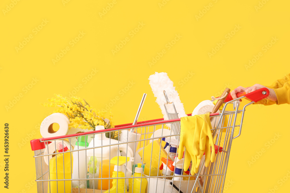 Woman with shopping cart full of cleaning supplies with flowers on yellow background