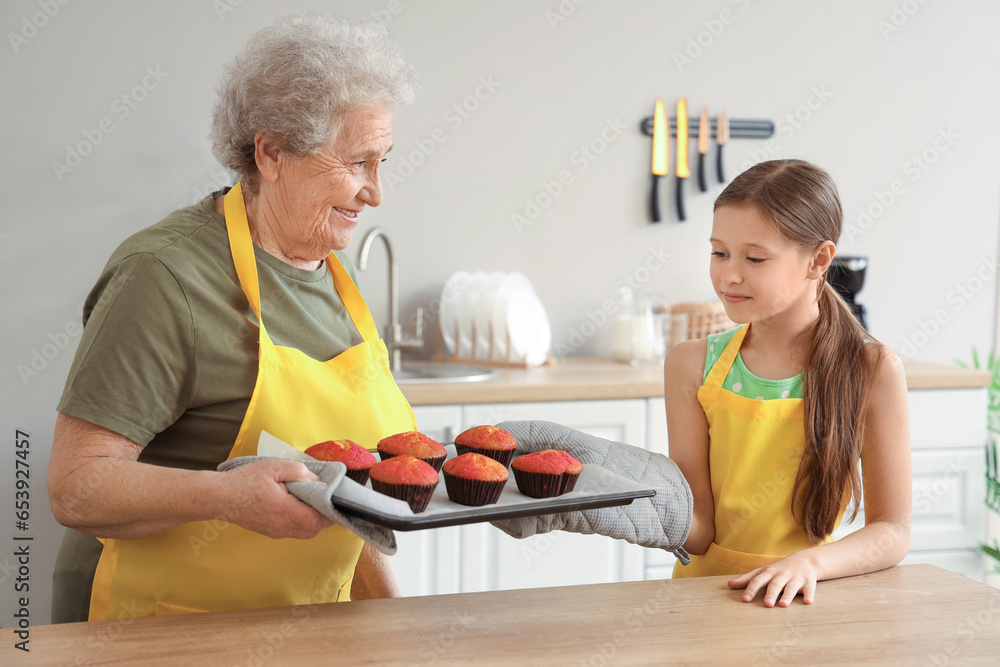 Little girl and her grandmother with prepared muffins in kitchen