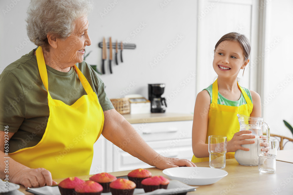 Senior woman and her little granddaughter with jug of milk in kitchen