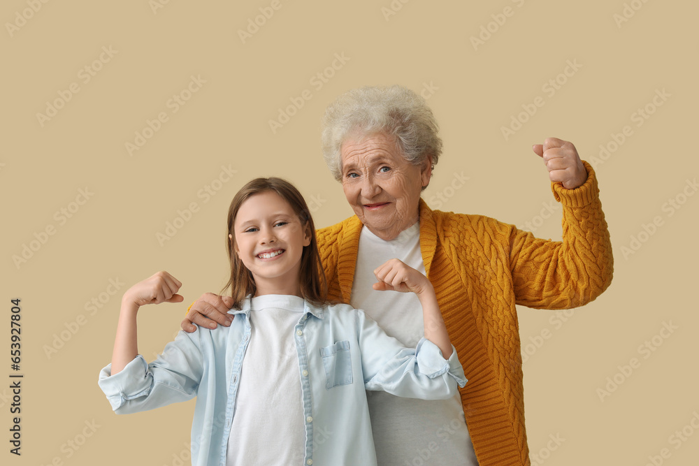 Little girl with her grandmother showing muscles on beige background