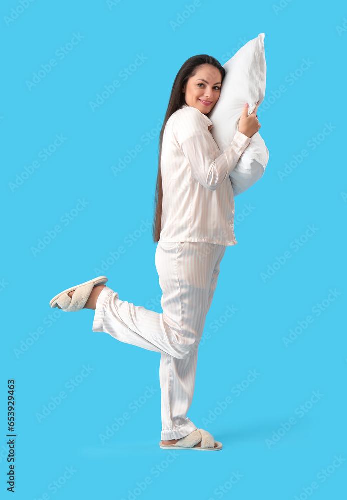 Pretty young woman with soft pillow on blue background