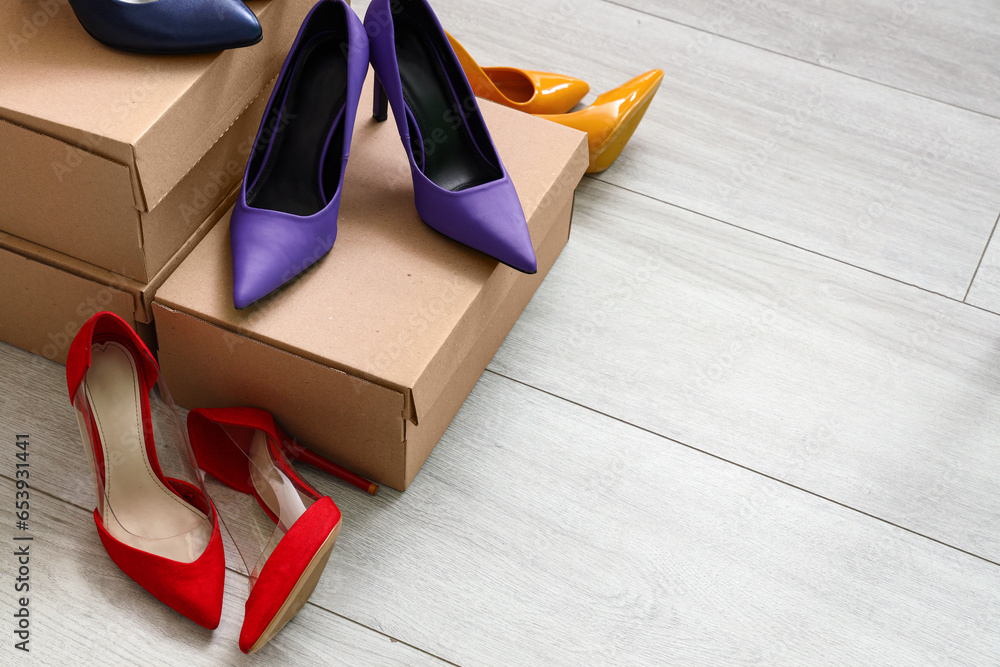 Cardboard boxes with different colorful high-heeled shoes on light wooden background