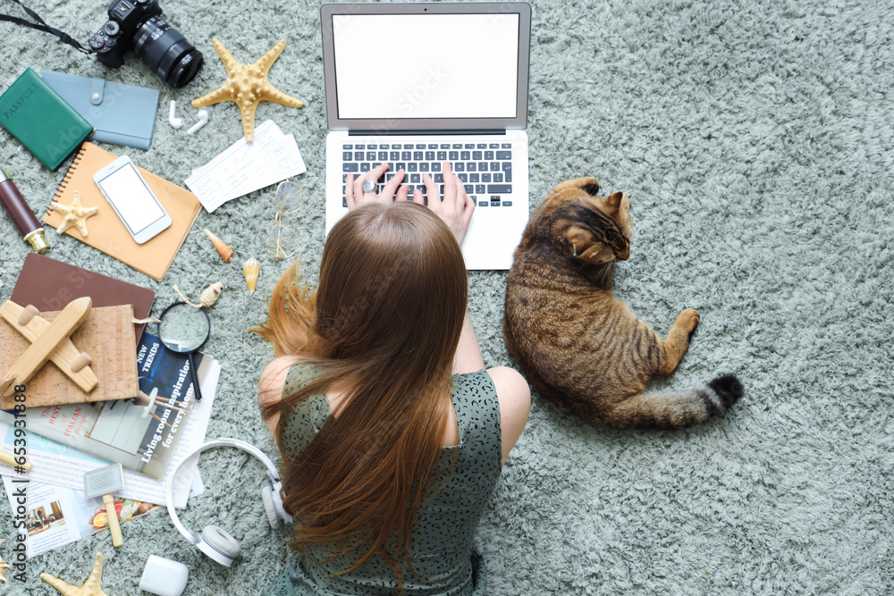 Woman with Scottish fold cat and travelling accessories using laptop on green carpet, top view