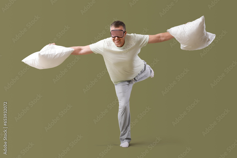 Mature man in sleeping mask with soft pillows on green background