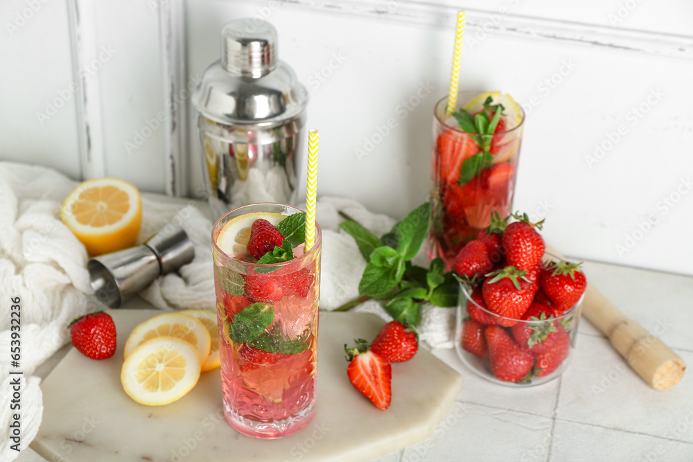 Glass of fresh strawberry mojito with shaker and jigger on white tile table