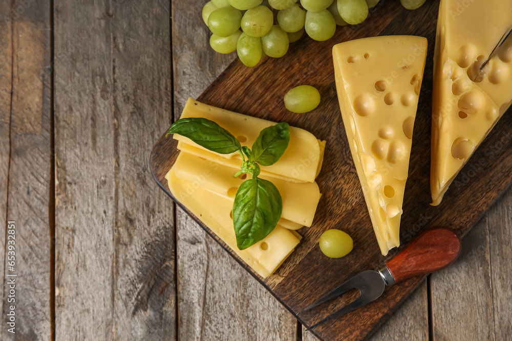 Board with tasty Swiss cheese and grapes on wooden background