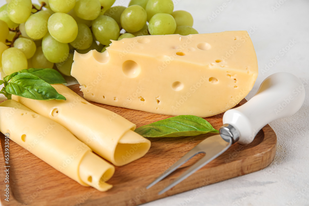 Wooden board with tasty Swiss cheese and grapes on light background