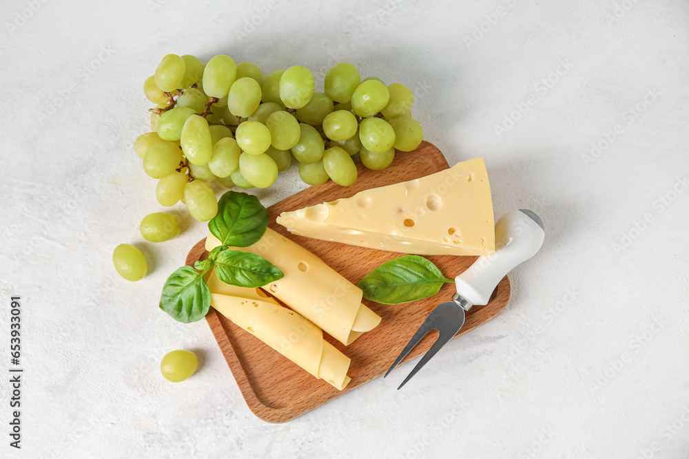 Wooden board with tasty Swiss cheese and grapes on light background