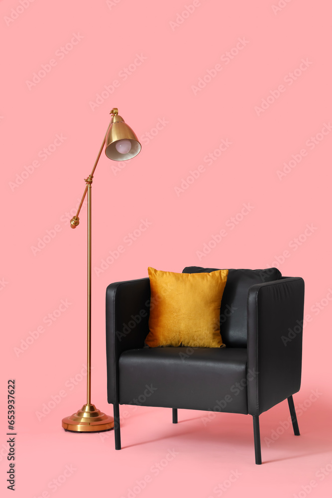 Black armchair with cushion and lamp on pink background