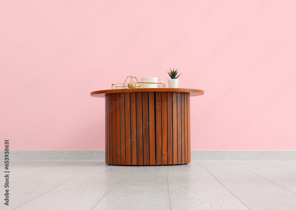 Wooden coffee table with houseplant, tray and cup near pink wall