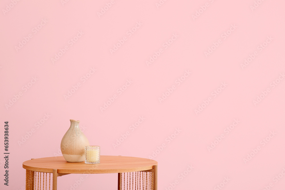 Wooden coffee table with vase and candle near pink wall