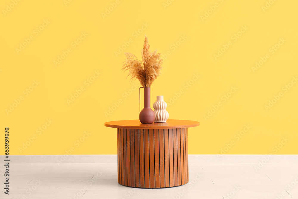 Wooden coffee table with pampas grass in vase near orange wall