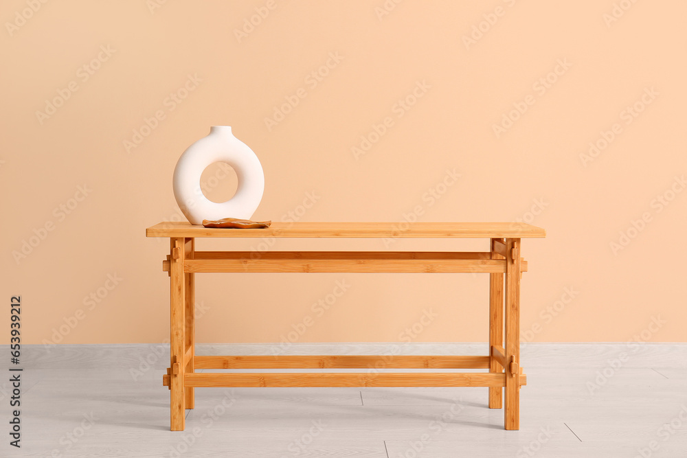 Wooden table with empty vase near beige wall