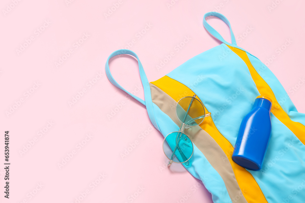 Stylish swimsuit, sunglasses and bottle of sunscreen cream on pink background