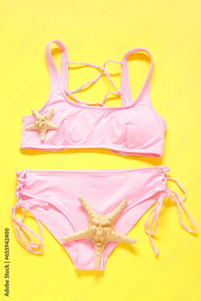 Stylish swimsuit and starfishes on yellow background