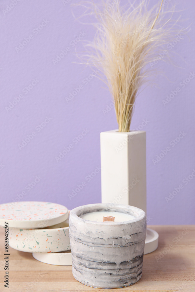 Holders with candles and pampas grass on wooden table near purple wall in room, closeup