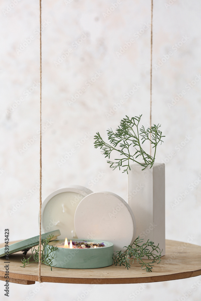 Fir tree branches and burning candle on hanging shelf near light wall in room, closeup