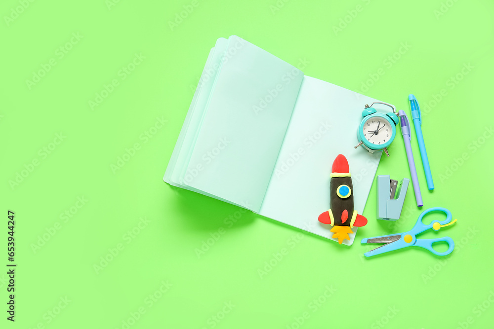 Blank notebook with rocket made of plasticine and different stationery on green background