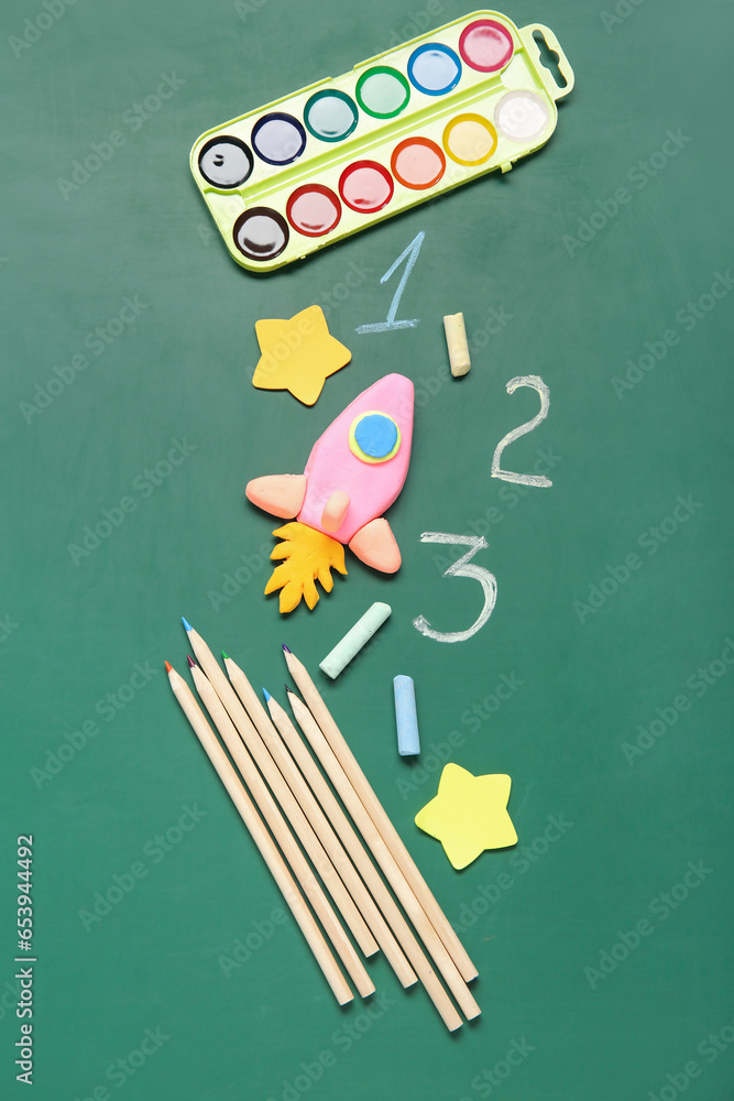 Rocket made of plasticine with different stationery on green chalkboard