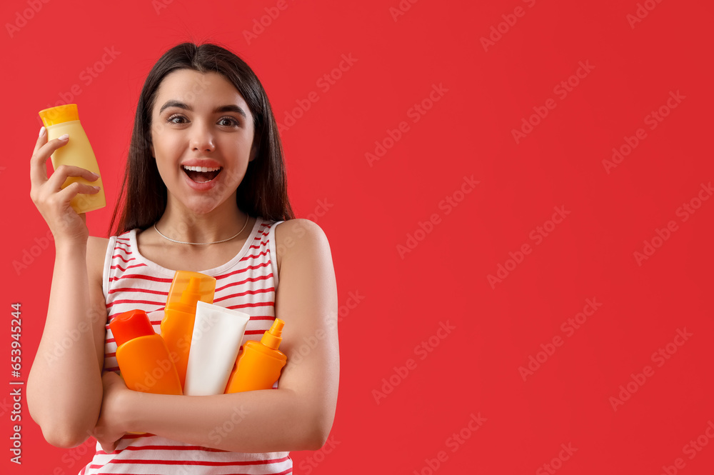 Young woman with bottles of sunscreen cream on red background