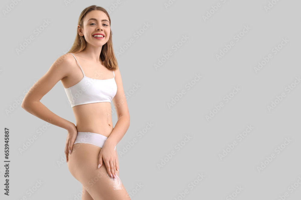 Young woman applying anti-cellulite cream on her leg against light background