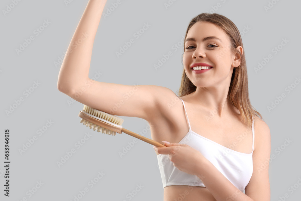 Young woman massaging her arm with anti-cellulite brush on light background