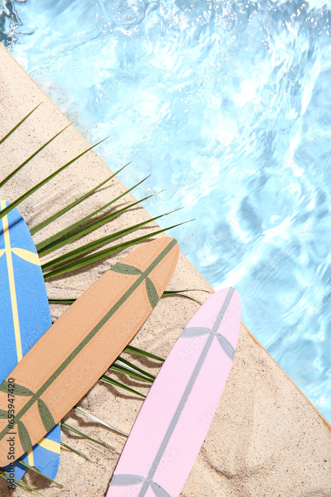 Different mini surfboards with palm leaf on sand near water