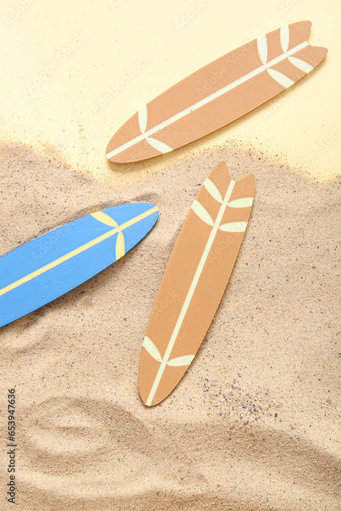 Mini colorful surfboards on sand against pale yellow background