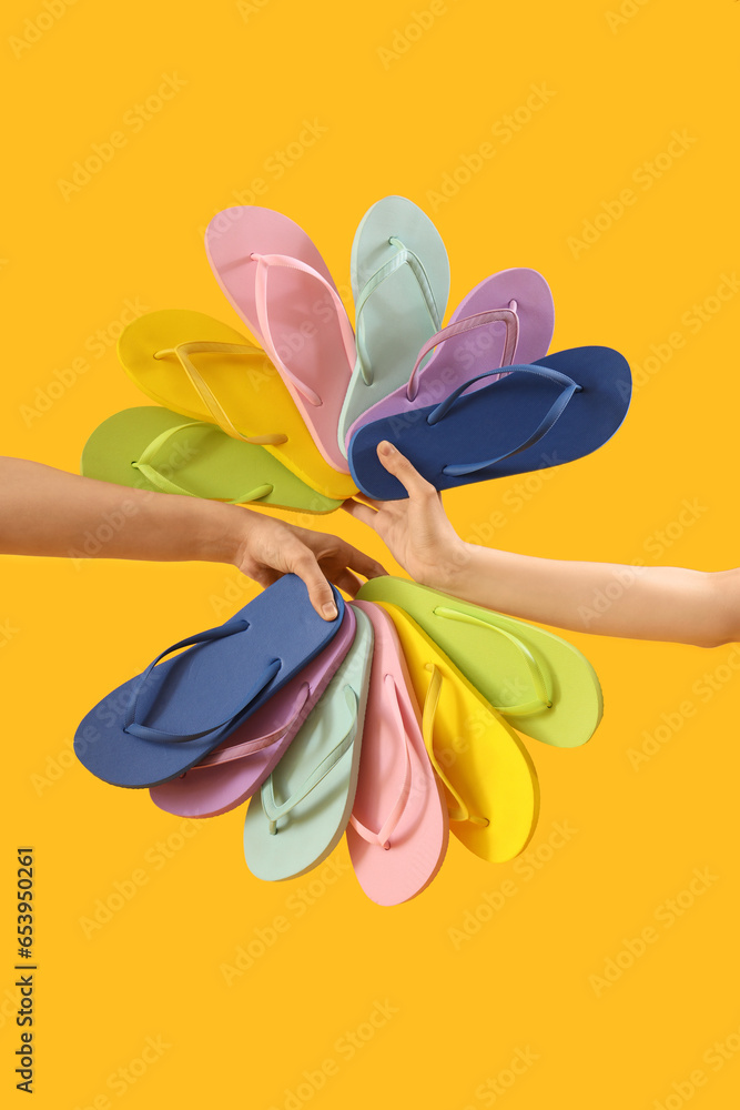 Hands with many flip-flops on yellow background