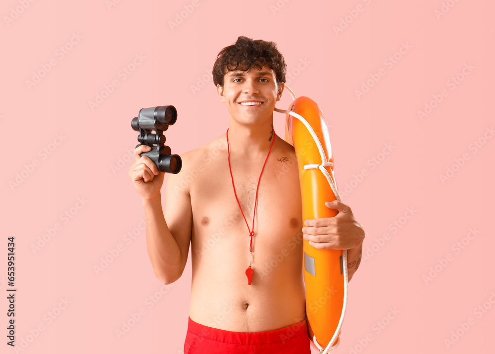 Male lifeguard with binoculars and ring buoy on pink background