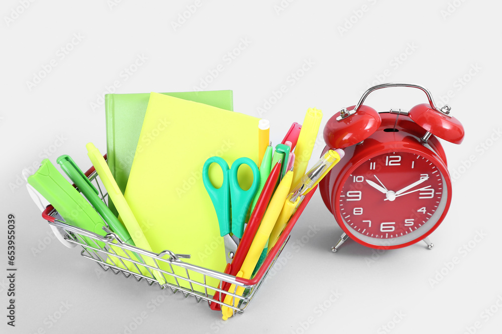 Alarm clock and shopping basket with different stationery on white background