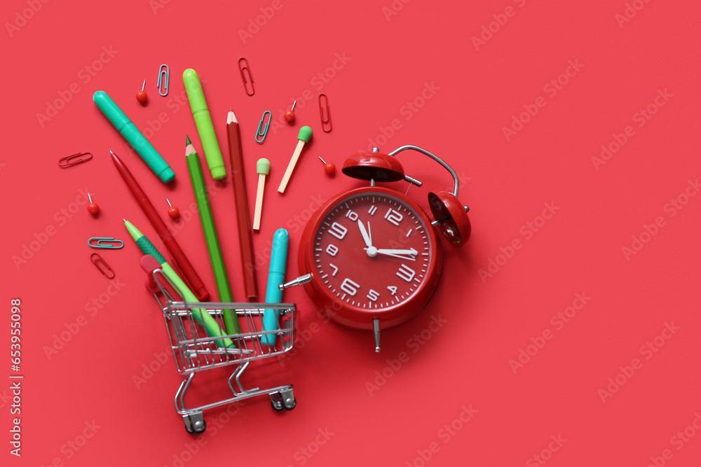 Alarm clock and shopping cart with different stationery on red background