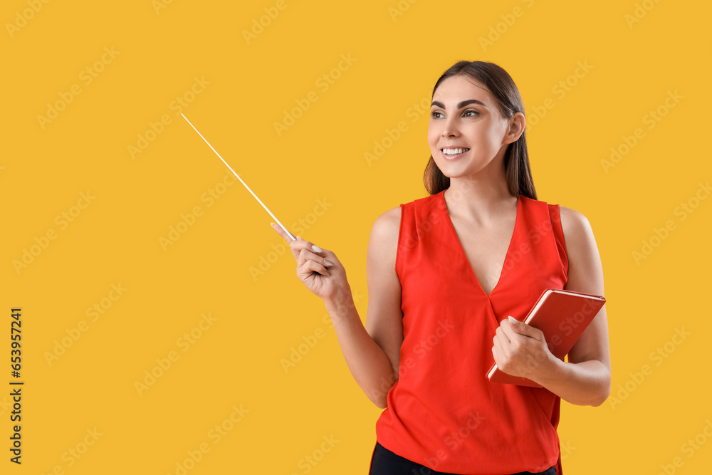 Young female teacher with pointer and notebook on yellow background