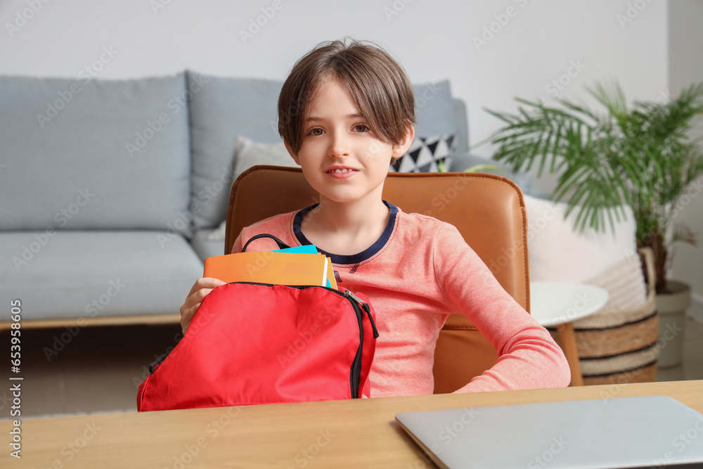 Little boy packing his schoolbag and sitting at table in living room