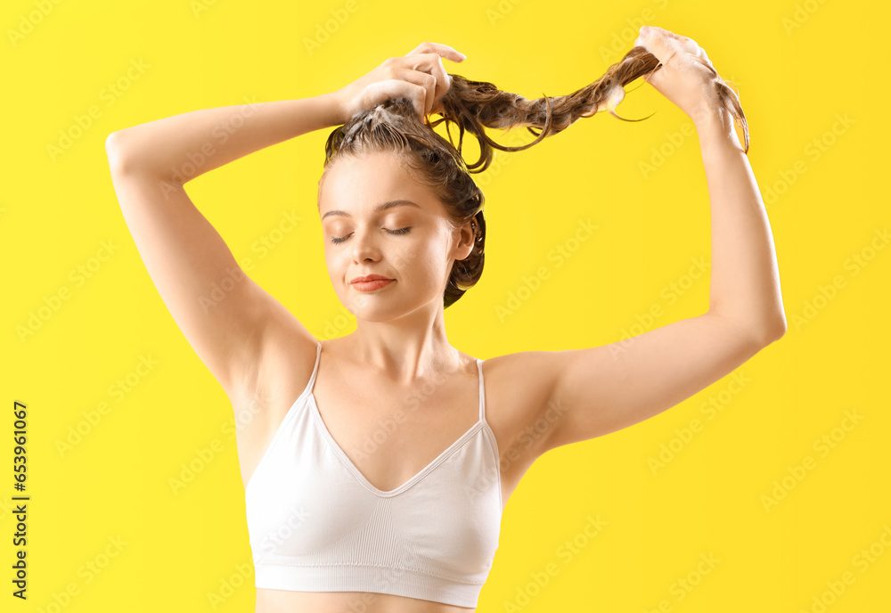 Young woman washing hair on yellow background