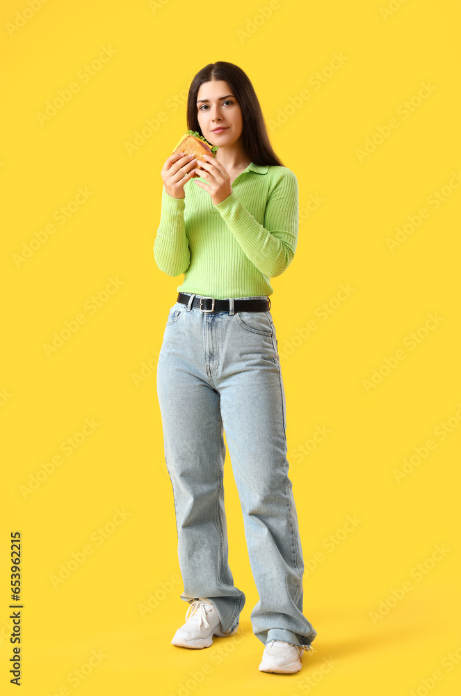 Young woman with tasty sandwich on yellow background