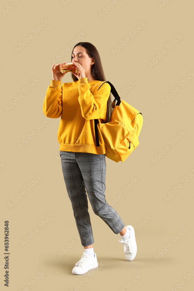 Female student eating tasty sandwich on green background