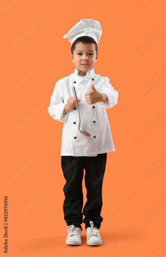 Cute little chef with ladle showing thumb-up on orange background