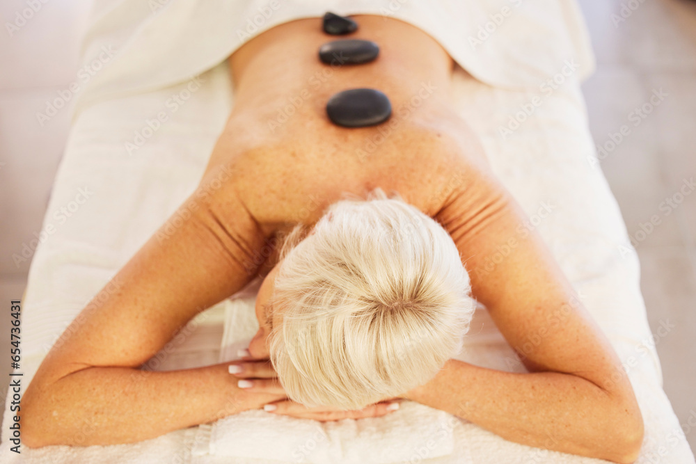 Senior woman, spa and wellness with stone, massage and relax with health, stress relief and luxury. Salon treatment, elderly person and pensioner with care, resting and spine with beauty and rock