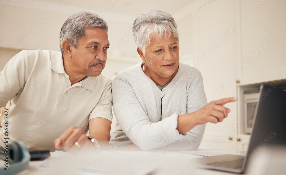 Senior couple, laptop and pointing in budget planning, finance or retirement together at home. Mature man and woman in serious discussion or investment on computer with financial documents in kitchen