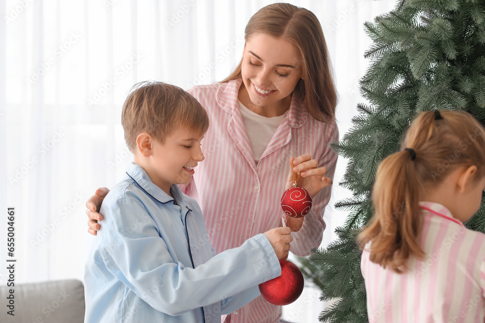 Happy mother with her little son decorating Christmas tree at home