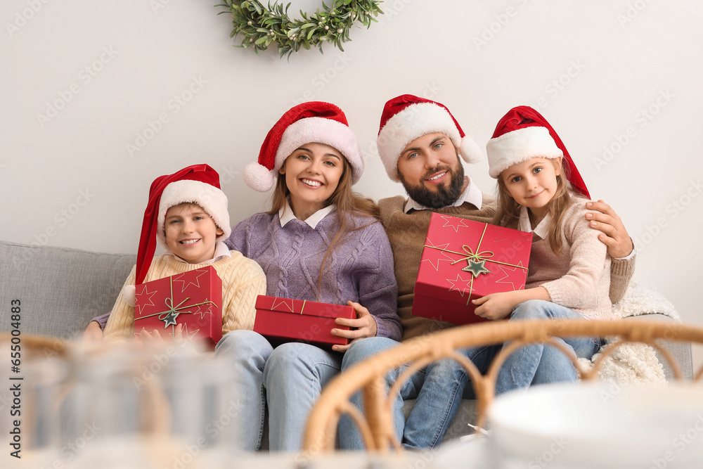 Happy family in Santa hats with Christmas gifts sitting on sofa at home