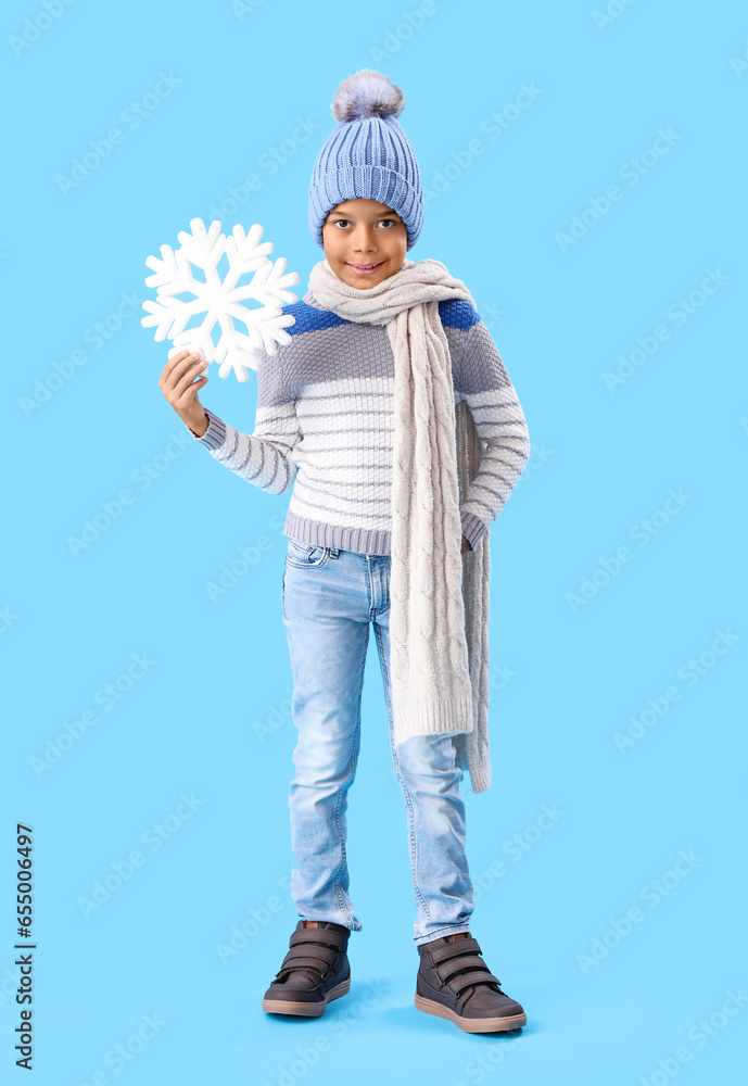 Cute African-American boy in warm winter clothes and with snowflake on blue background