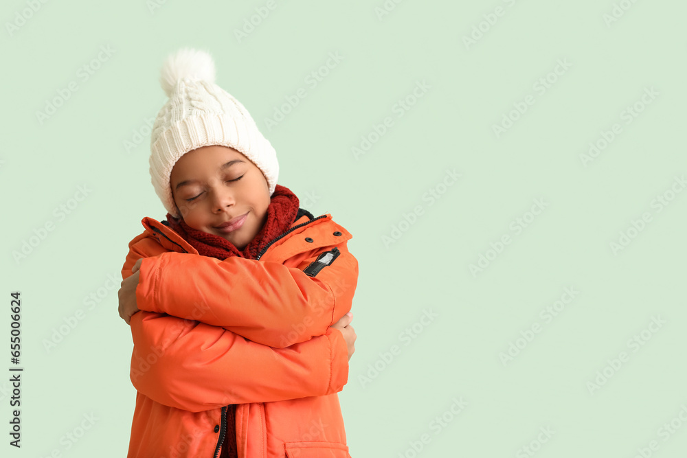 Cute African-American boy in warm winter clothes on light background