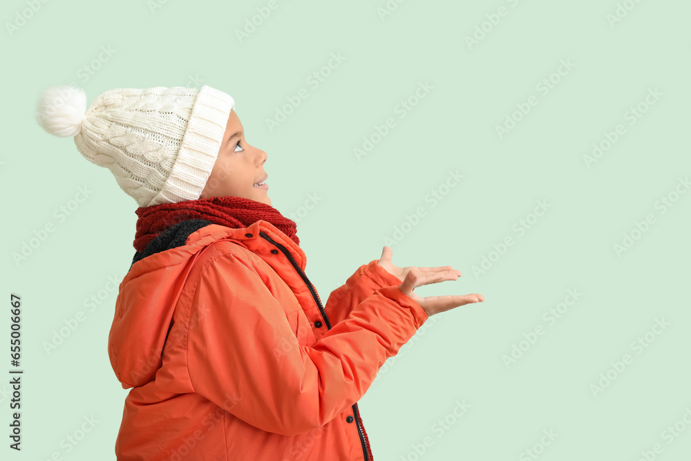 Cute African-American boy in warm winter clothes on light background