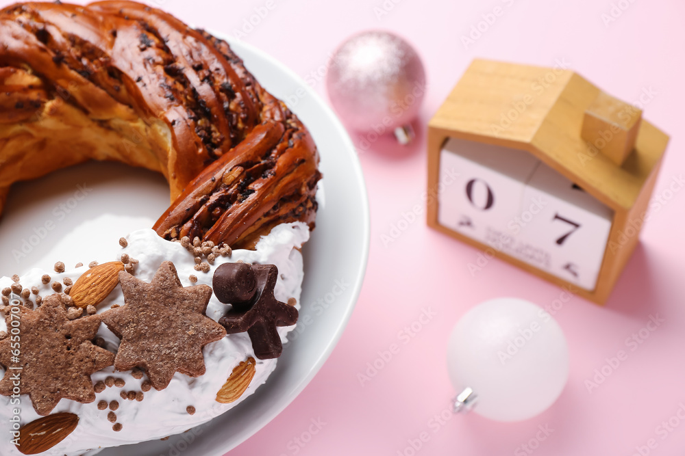 Plate with pastry wreath, Christmas balls and cube calendar on pink background