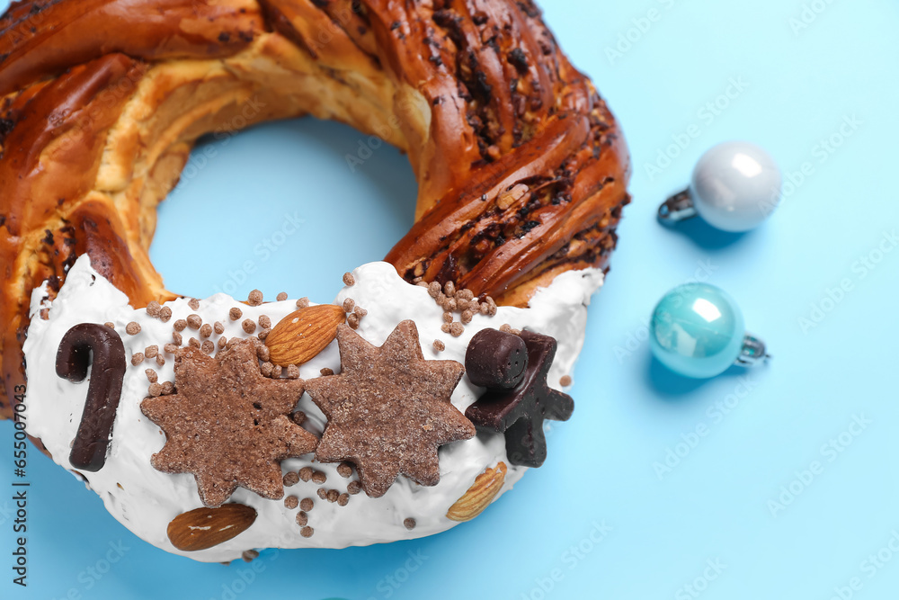 Tasty pastry wreath with Christmas balls on blue background, closeup